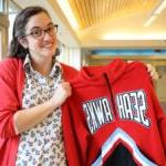 Chief Sealth Teacher Sarah Martin standing in the high school holding a sweatshirt with 