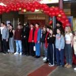A group of students stand below a red balloon arch in a school hallway